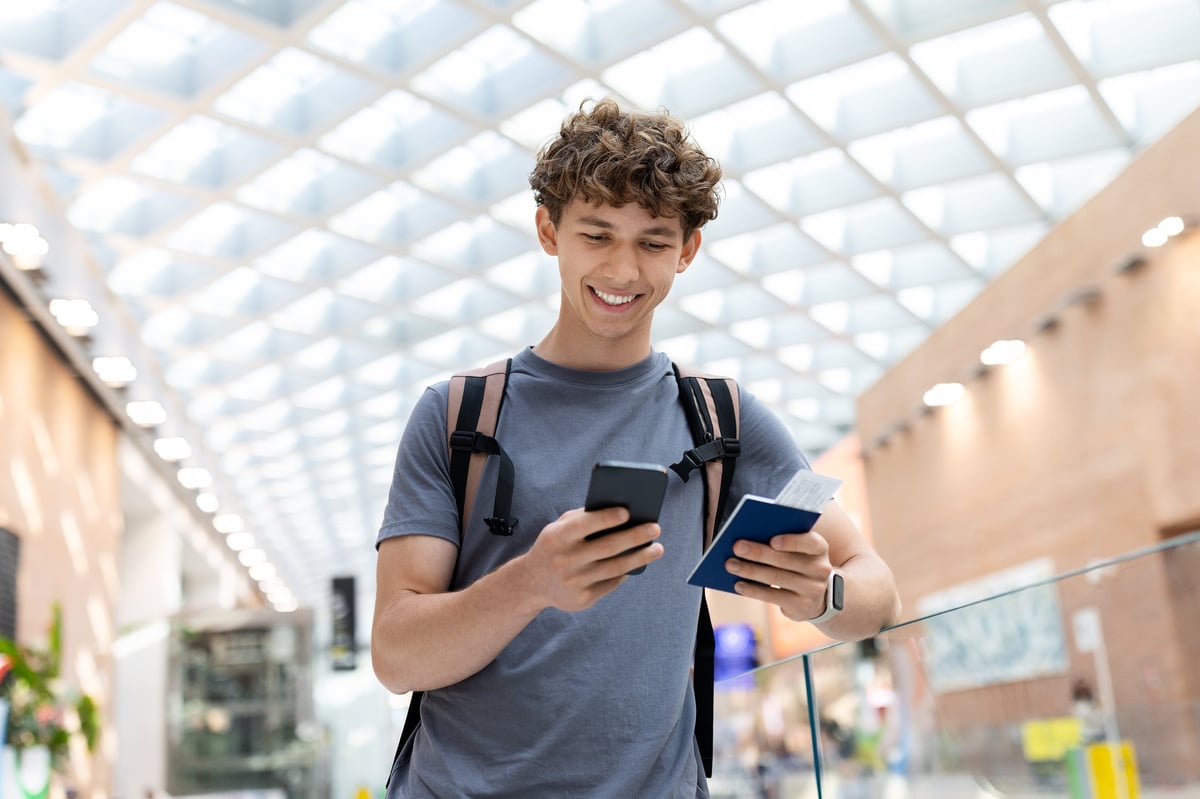 Joven sonriendo sosteniendo pasaporte y teléfono en un aeropuerto, concepto de viaje y visa