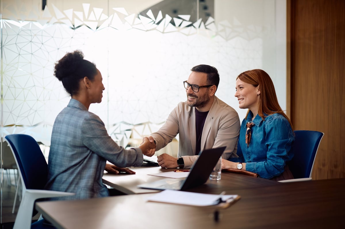 Happy couple shaking hands with their insurance agent in the office, professional consultation